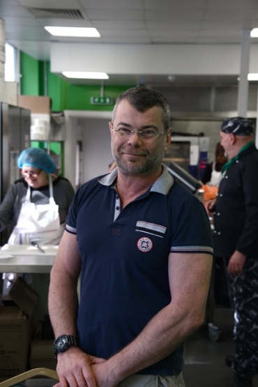 Man standing in busy kitchen, smiling at camera