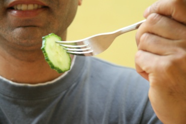 Close up of man holding forked cucumber slice, smiling